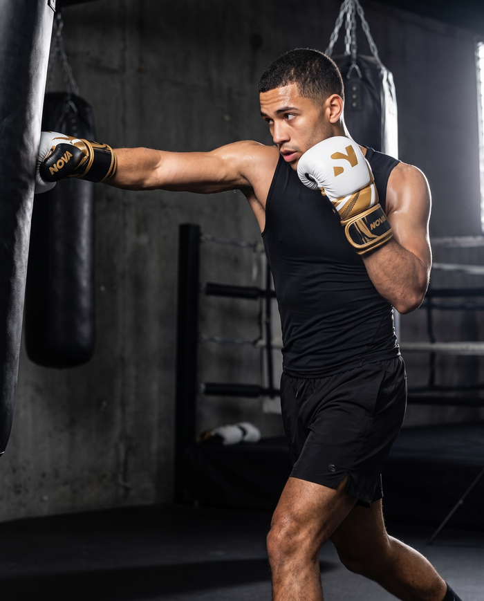Model throwing a punch on a heavy bag wearing NOVA white, black and gold boxing gloves — Gloves available in Mauritius
